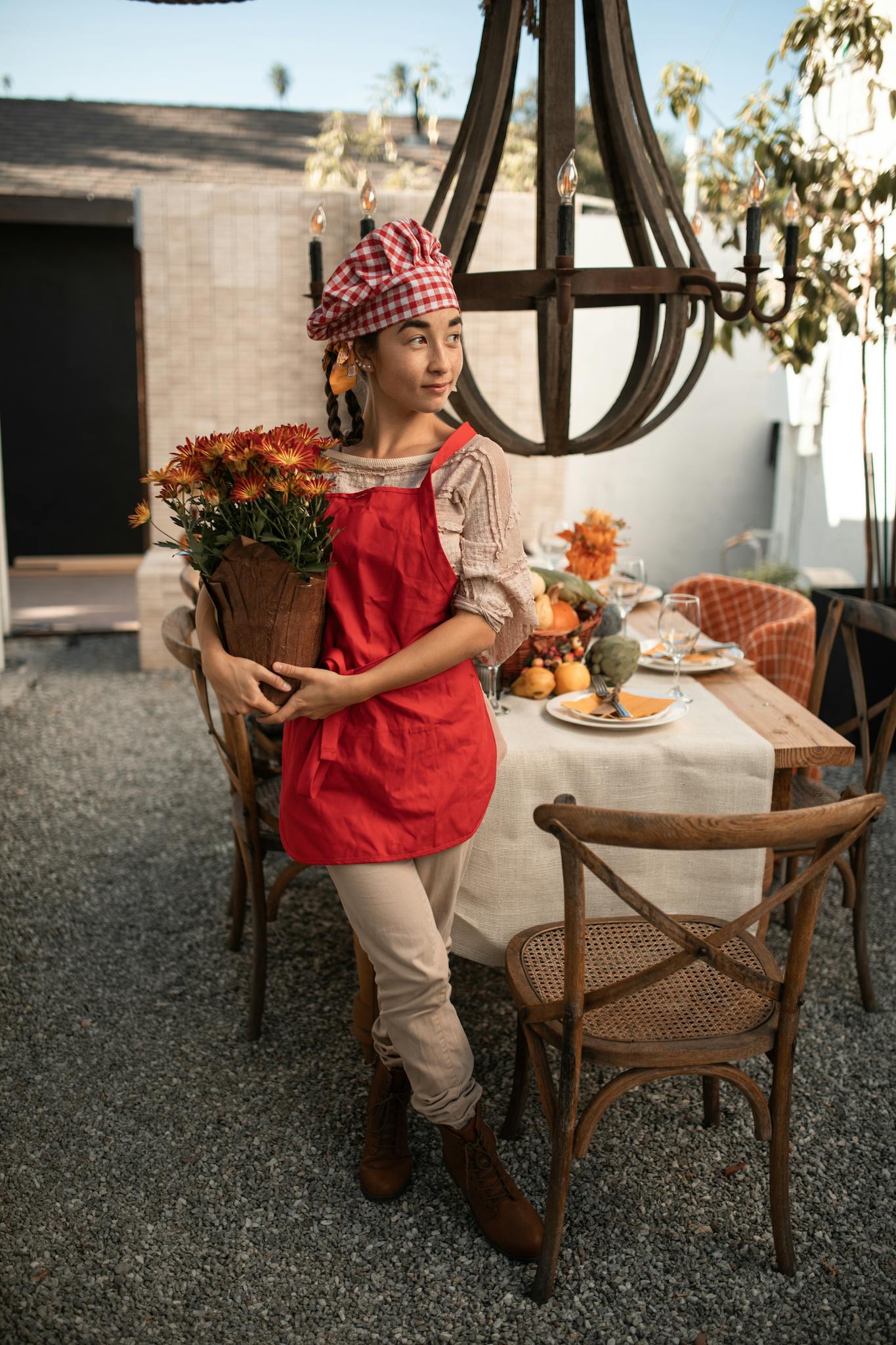 A young woman in a fall-themed setting holds flowers during a festive outdoor family gathering.