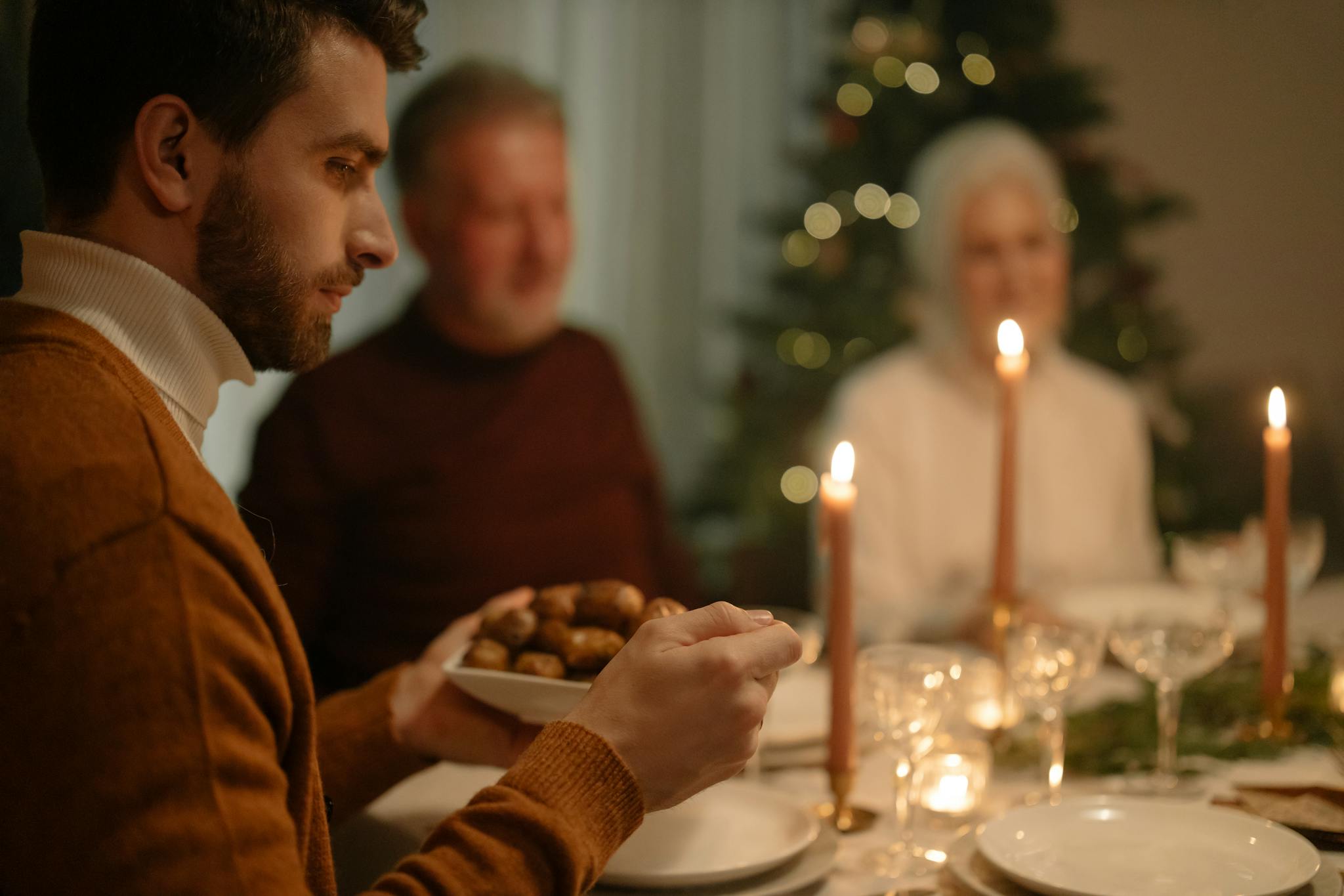Warm family dinner scene with candles and holiday tree, evoking festive joy.